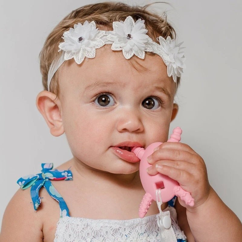 Baby using The Molar Magician Teether in Pink on a light gray background. 