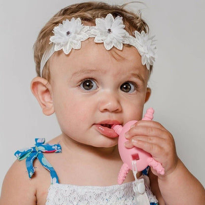Baby using The Molar Magician Teether in Pink on a light gray background. 