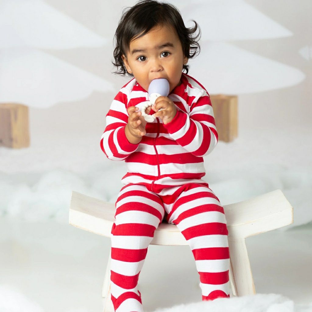 Baby holding The Teething Egg attached to the Grippy Stick on a white background. 