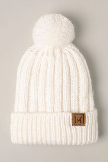 White knit beanie pom-pom hat laying on a light gray background.