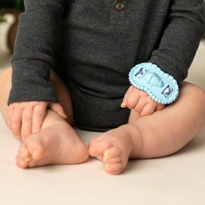 Baby wearing blue wrist Wristie Teether on wrist sitting in gray onesie on a beige surface. 