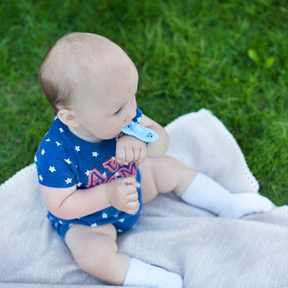 Baby sitting outdoors on blanket using blue wrist Wristie teether.